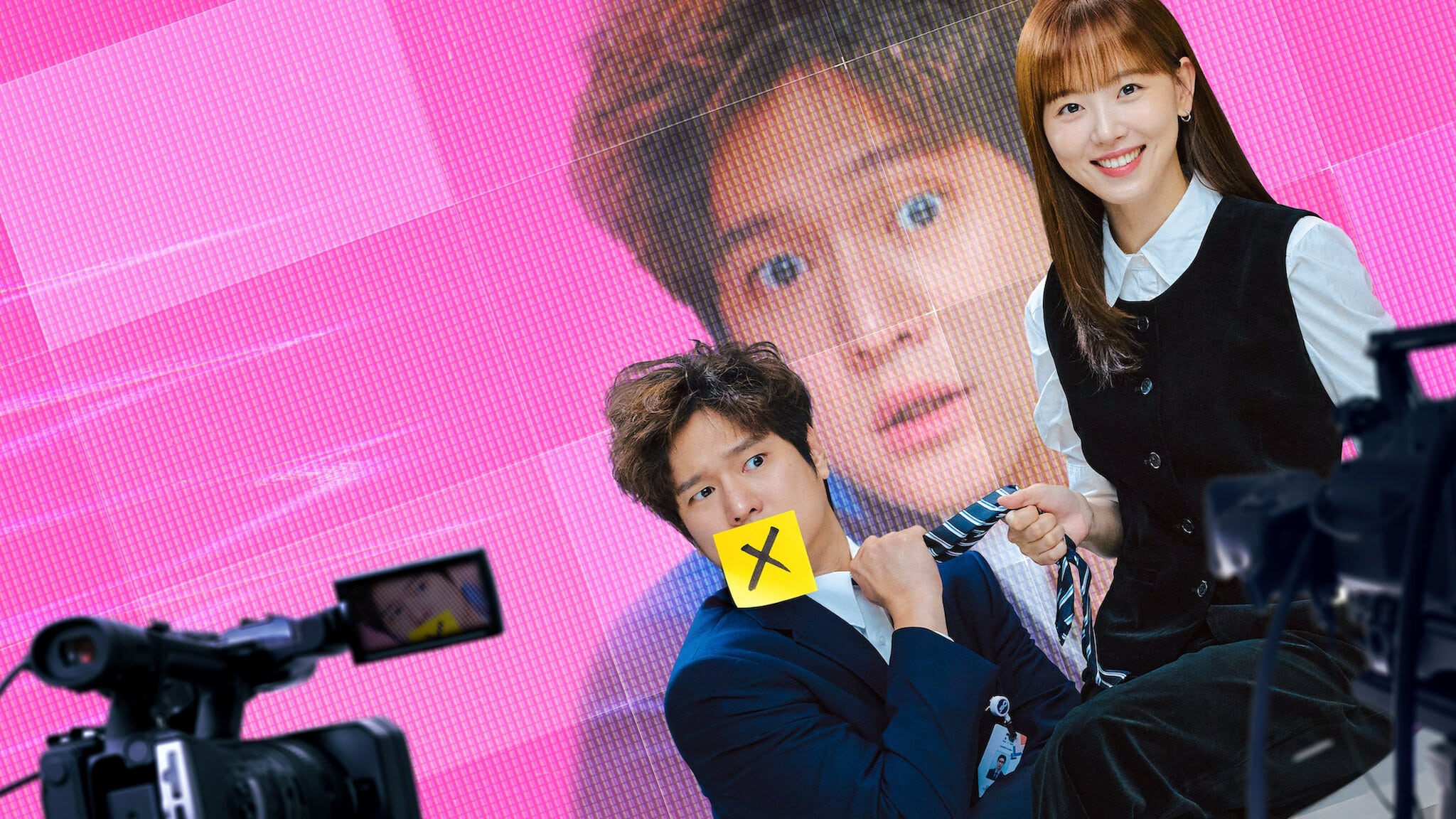 Hai diễn viên Hàn Quốc tươi cười trước phông nền màn hình lớn và thiết bị quay phim