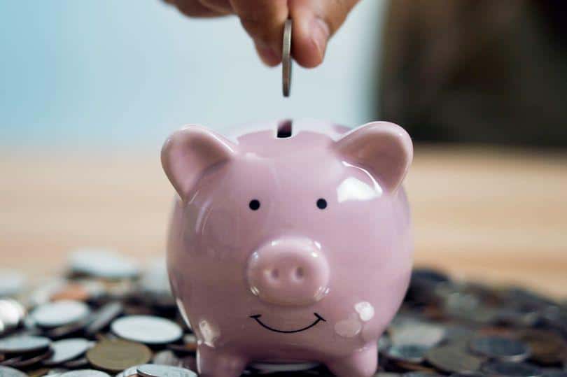 Tay đang bỏ đồng xu vào heo đất đặt trên bàn với nhiều tiền xu xung quanh